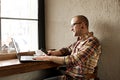 Smiling bearded businessman wearing casual hipster clothing using laptop and cell smartphone in coffe house. Royalty Free Stock Photo