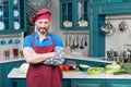 Smiling bearded Chef with tattooed hand in red apron and red hat on kitchen