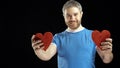 Smiling bearded man in blue tshirt holds two red heart shapes. Love, romance, dating, relationship concepts. Black Royalty Free Stock Photo