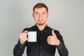 A smiling bearded man holds a large white cup in his hands and shows a thumbs up gesture while standing on a gray background Royalty Free Stock Photo