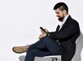 Smiling bearded man in jeans and stylish casual tweed jacket is using his smartphone messaging reading news. Side view Royalty Free Stock Photo