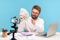 Smiling bearded man life coach holding fan of dollars and pointing finger on you, recording video on smartphone camera, teaching Royalty Free Stock Photo