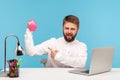 Smiling bearded man office worker pointing at dumbbell, showing how he is pumping muscles sitting at workplace with laptop, go in Royalty Free Stock Photo