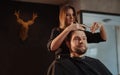 Smiling bearded Man portrait enjoying hairstyle hairdressing in Hair Salon by young hairdresser female. Modern low light black Royalty Free Stock Photo