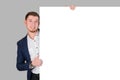 A smiling bearded man shows a thumbs up gesture while holding onto a white blank board, standing on a gray background Royalty Free Stock Photo