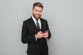 Smiling bearded man in suit using his smartphone