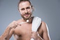 Smiling bearded man with towel on shoulder holding toothbrush with toothpaste in hand, Royalty Free Stock Photo