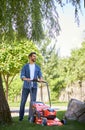 Smiling bearded man trimming lawn with modern mower, while working in garden at sunny day. Royalty Free Stock Photo