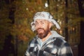 Smiling bearded ranger man in autumn fur cap with ear-flaps and plated warm jacket walking alone in cold autumn forest
