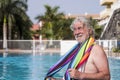 Smiling bearded senior man with white hair standing in the swimming pool with a colorful towel on shoulders - active elderly Royalty Free Stock Photo