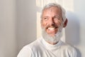 Smiling bearded senior old man laughing standing at white wall in sunlight. Royalty Free Stock Photo