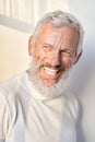 Smiling bearded senior older man laughing standing at white wall in sunlight. Royalty Free Stock Photo