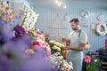 Smiling bearded young male in apron spraying roses in front of flower stand