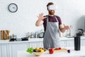 smiling bearded young man in apron using virtual reality headset while cooking in kitchen Royalty Free Stock Photo