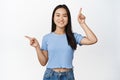Smiling beautiful asian girl shows two products on sale, pointing sideways, standing in blue tshirt over white