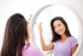 Smiling beautiful asian woman looking at herself in the mirror at home