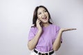 Smiling beautiful Asian woman pointing finger sideward to space while picking up phone call isolated white background