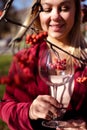 Smiling beautiful blond woman stands with a glass of wine in the sun on the background of rowan branches. Autumn Royalty Free Stock Photo