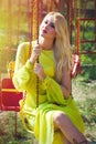 Beautiful blonde fashion woman in long elegant yellow dress sit on flying carousel in amusement park summer