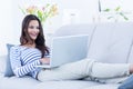 Smiling beautiful brunette relaxing on the couch and using her laptop