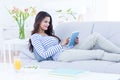 Smiling beautiful brunette relaxing on the couch and using her tablet Royalty Free Stock Photo