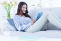 Smiling beautiful brunette relaxing on the couch and using her tablet Royalty Free Stock Photo