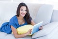 Smiling beautiful brunette relaxing on the couch and using her tablet Royalty Free Stock Photo