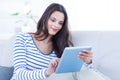 Smiling beautiful brunette relaxing on the couch and using her tablet Royalty Free Stock Photo