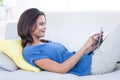 Smiling beautiful brunette relaxing on the couch and using her tablet Royalty Free Stock Photo
