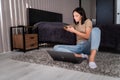 Smiling beautiful brunette sitting on the floor and using her phone in the living room. Working from home in quarantine lockdown. Royalty Free Stock Photo