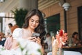 Smiling beautiful brunette young woman in white clothes using mobile phone on table at terrace of summer cafe Royalty Free Stock Photo