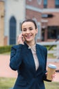 smiling beautiful businesswoman talking by smartphone and holding coffee Royalty Free Stock Photo