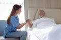 Smiling beautiful caring female doctor holding hand of male senior patient who lying in hospital bed. Nurse takes care elderly man Royalty Free Stock Photo
