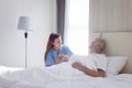 Smiling beautiful caring female doctor holding hand of male senior patient who lying in hospital bed. Nurse takes care elderly man Royalty Free Stock Photo