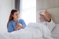 Smiling beautiful caring female doctor holding hand of male senior patient who lying in hospital bed. Nurse takes care elderly man Royalty Free Stock Photo