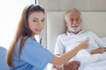 Smiling beautiful caring female doctor using stethoscope listen to senior patient heart who lying in hospital bed. Nurse takes