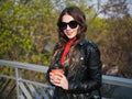 Smiling beautiful cheerful brown haired curly teen model in red dress holding take away coffee cup enjoying warm spring day at Royalty Free Stock Photo