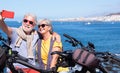 Smiling beautiful elderly couple sitting on the cliff taking a selfie with smartphone. Active retirees enjoying healthy lifestyle