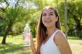 Smiling beautiful fitness woman have a break from work out holding a bottle of water to drink looking away in city park Royalty Free Stock Photo