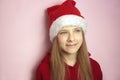 Smiling beautiful girl with long hair in fluffy Santa Claus hat on a pink background. Royalty Free Stock Photo