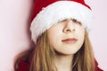 Smiling beautiful girl with long hair in fluffy Santa Claus hat on a pink background. Royalty Free Stock Photo