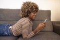 Smiling beautiful girl lying on a couch at home texting a with her smartphone. Happy young female using a mobile phone Royalty Free Stock Photo