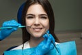 Smiling beautiful happy brunette woman patient examined by dentist in blue gloves using dental mirror and scaler during