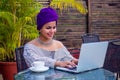 Smiling beautiful indian girl with ethnic turban on head culture working on laptop outdoors summer cafe Royalty Free Stock Photo