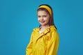 Cute girl wearing yellow raincoat with hood over blue wall, has good mood Royalty Free Stock Photo