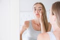 Smiling beautiful young woman looking into a mirror at herself in room. Beauty, hygiene, morning and people concept Royalty Free Stock Photo