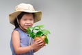 Smiling beautiful small Asian kid, wearing hat. Child holding a young tree seedling in coconut pot with clear background. Royalty Free Stock Photo