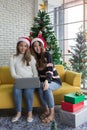 Smiling beautiful two women with sweater and santa hat holding laptop sitting on yellow sofa in christmas party Royalty Free Stock Photo