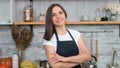 Smiling beautiful woman in apron posing with crossed hand at cosiness kitchen interior