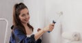 Smiling beautiful woman renovates apartment with boy paints walls white holding roller in hand last finishing touches